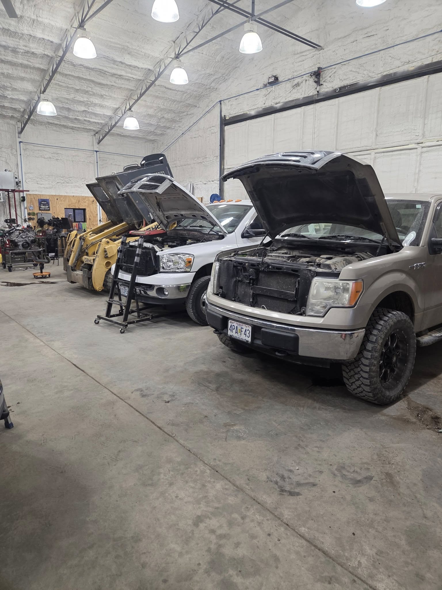 Two trucks with open hoods in a automotive shop setting.