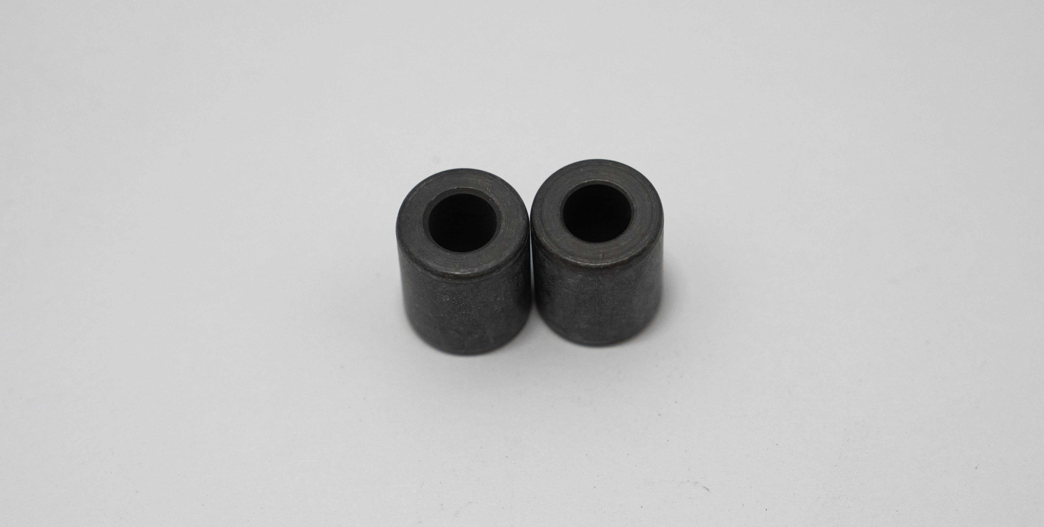 Two black cylindrical automotive spacers on a gray background