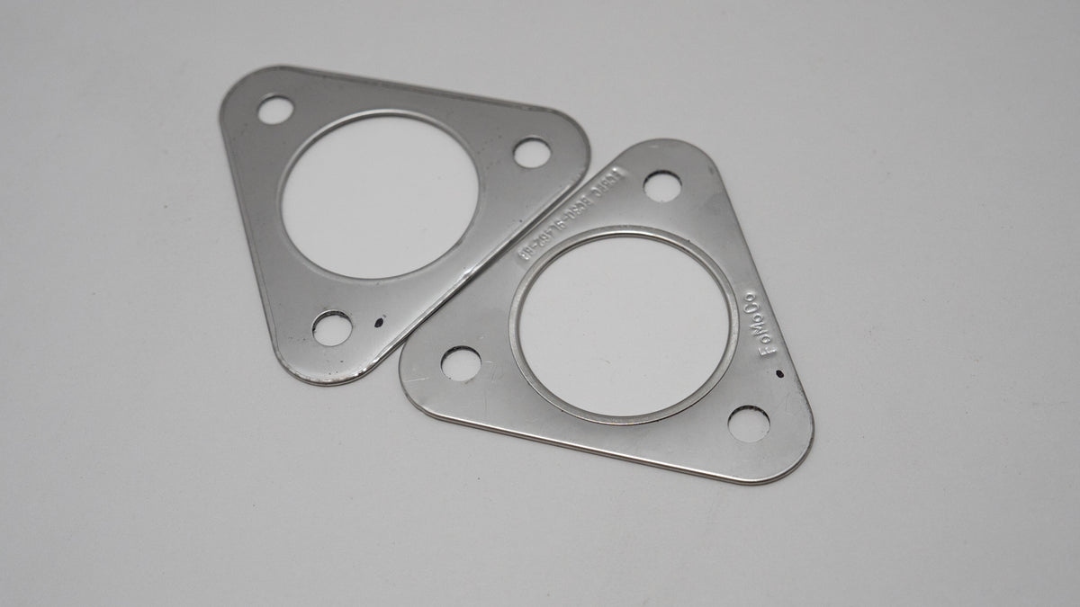 Two triangular metal automotive exhaust gaskets on a gray background