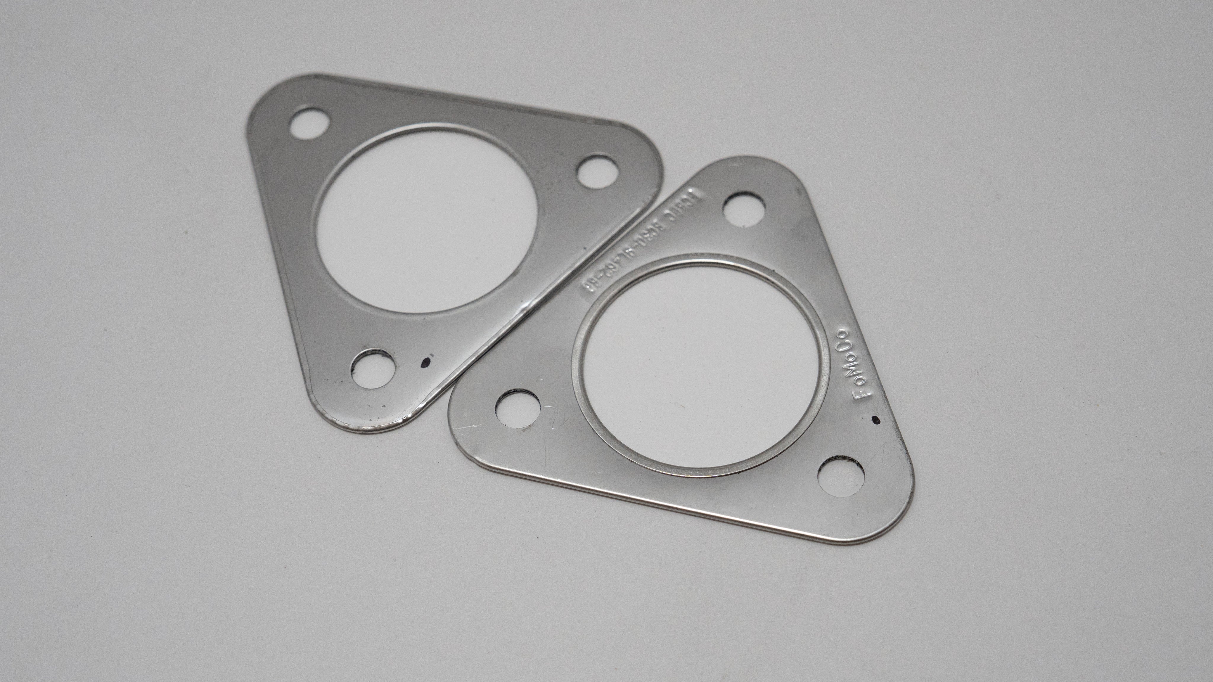 Two triangular metal automotive exhaust gaskets on a gray background