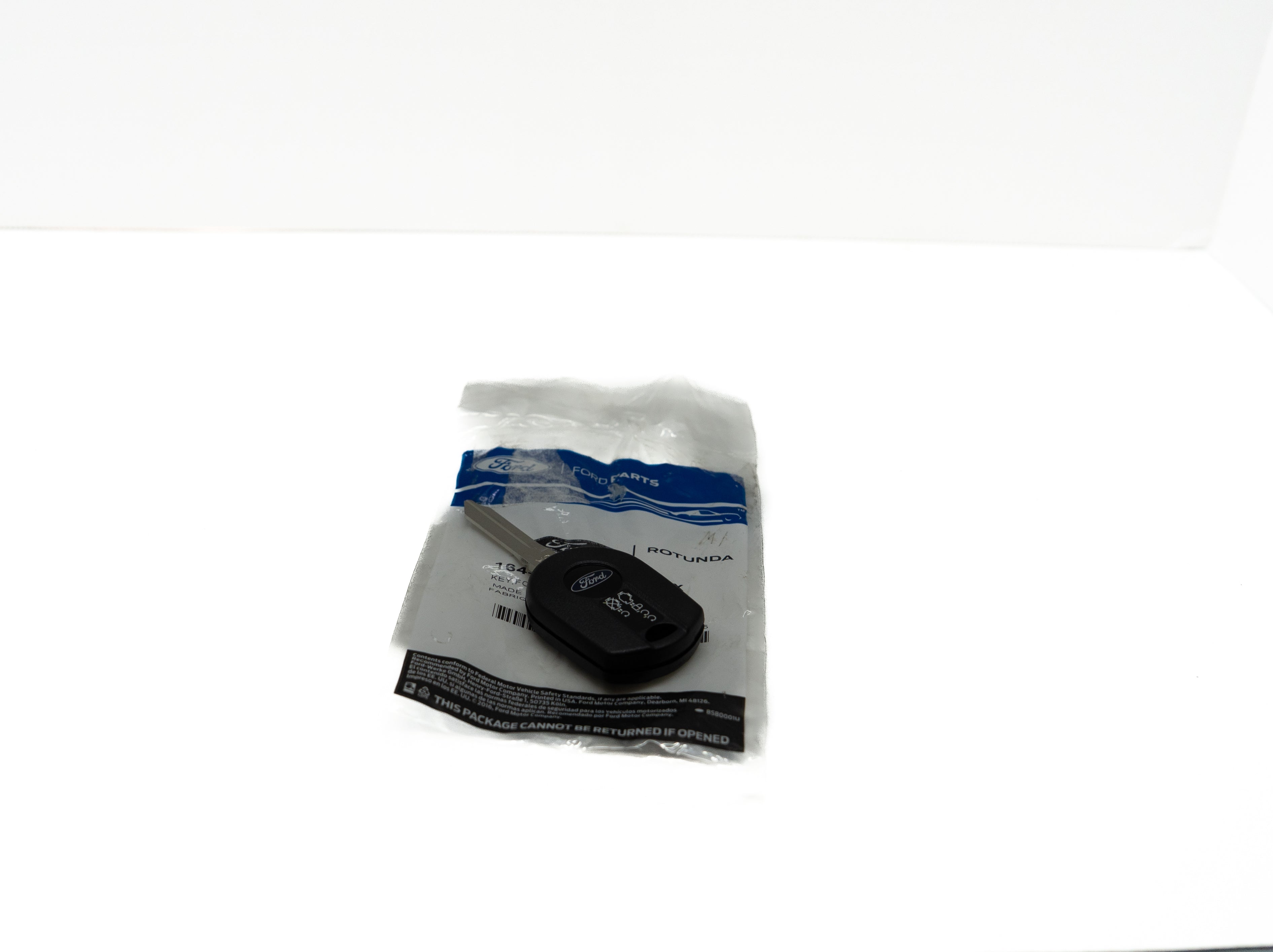 Black remote control automotive key fob in a clear plastic bag on a white background