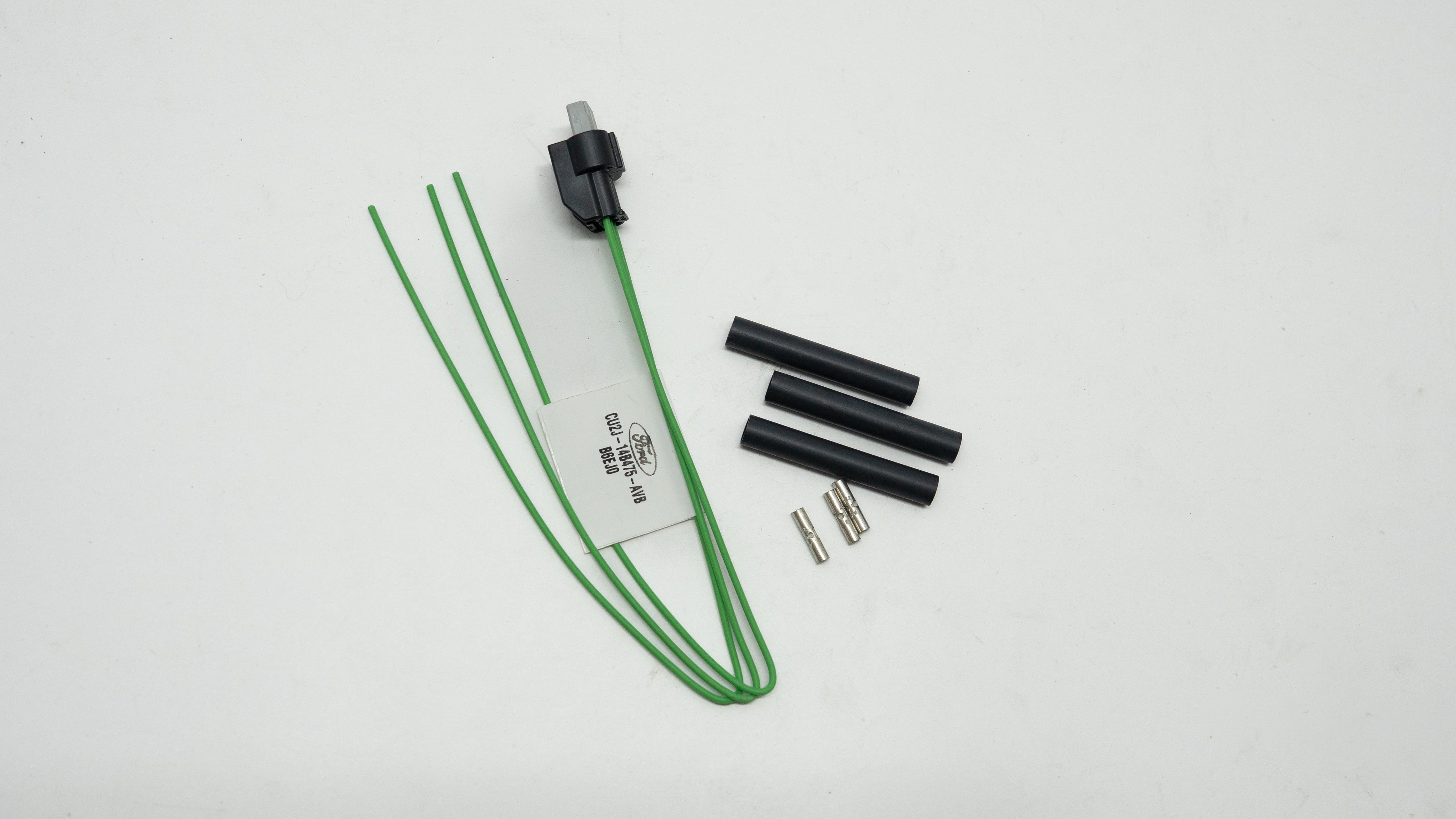 Electrical components including a green cable, black connectors, and a white label on a light gray background.