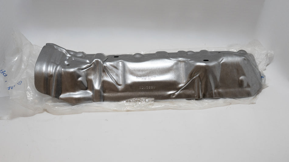 Metallic automotive heat shield plate component in clear plastic packaging on a white background.