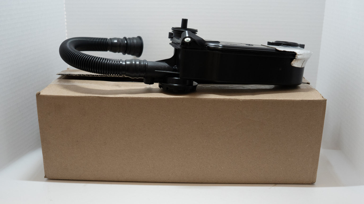Black engine oil / air separator valve and hose on product box on a white background.  
