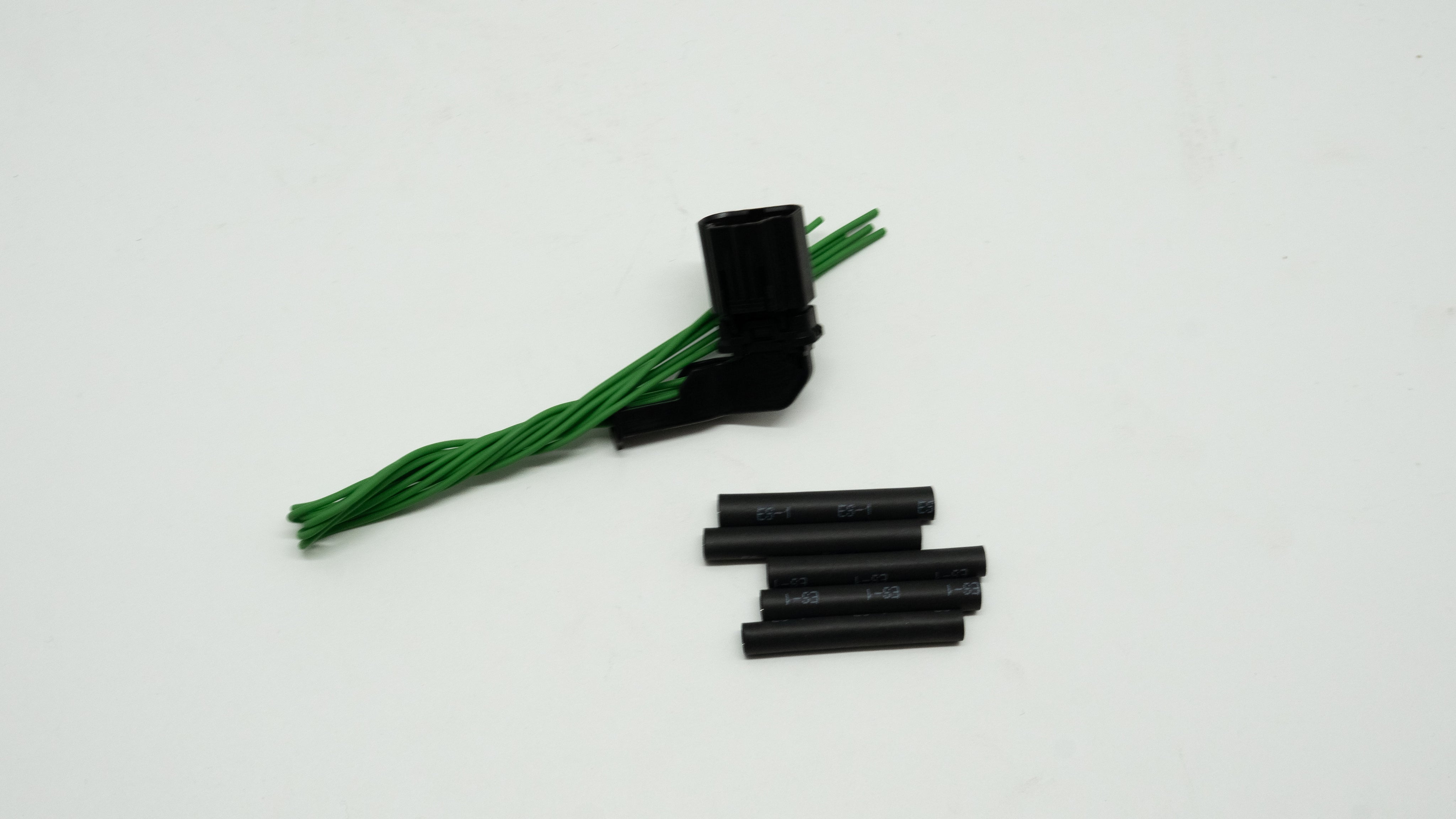 Black cylindrical objects and green braided wiring with connector on a white background