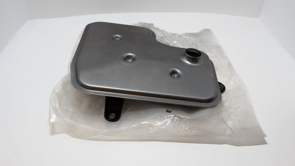 Silver transmission oil filter on plastic packaging with a white background. 