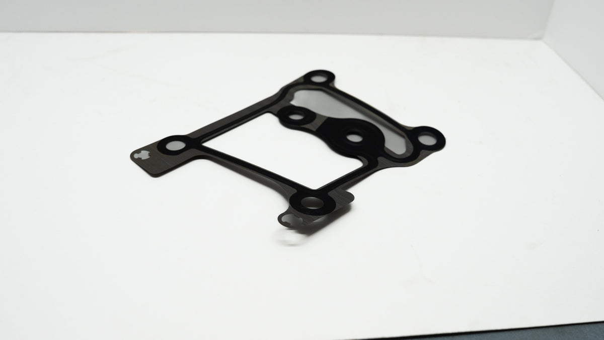 Black and grey automotive gasket on a white surface.