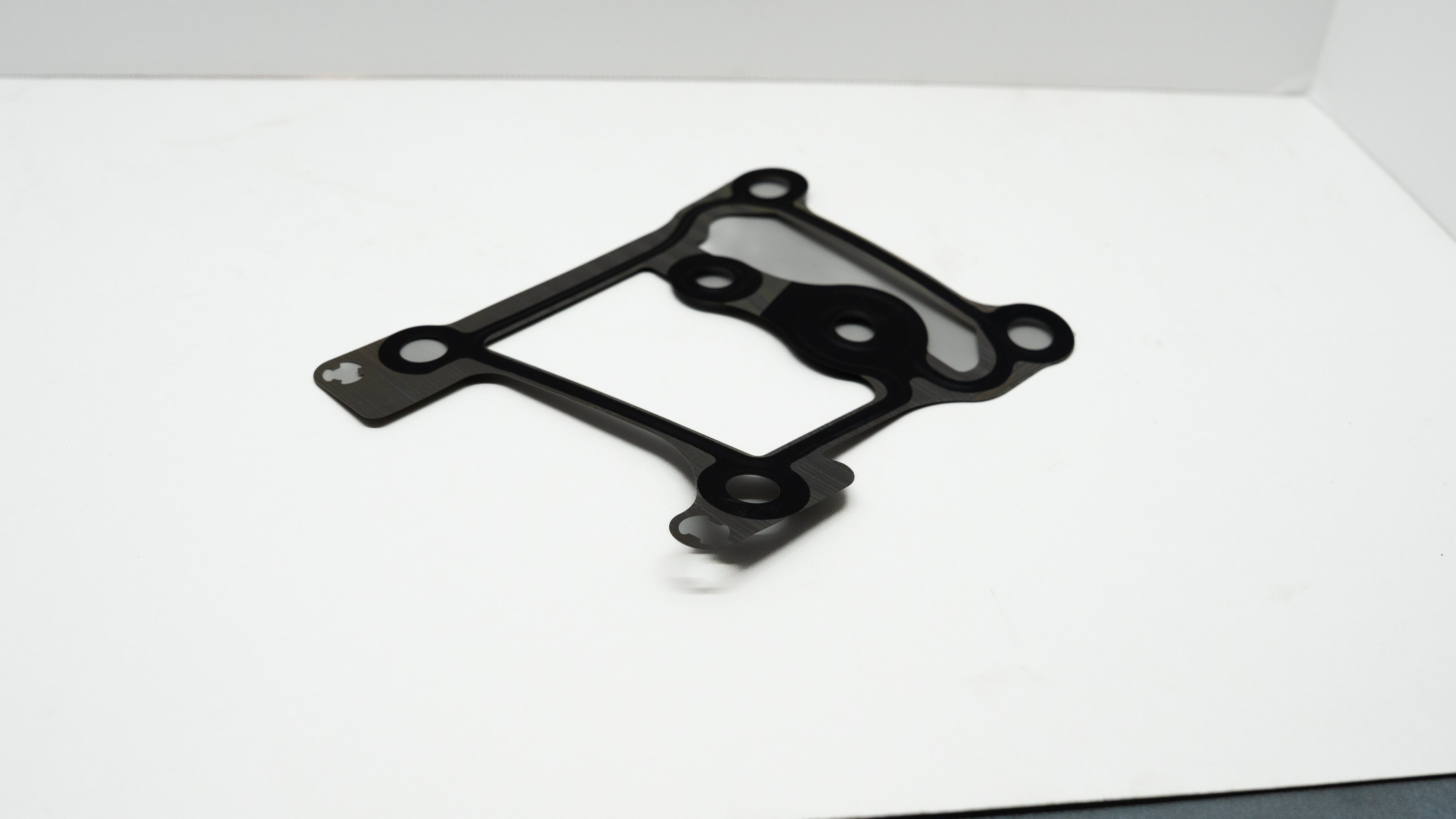 Black and grey automotive gasket on a white surface.