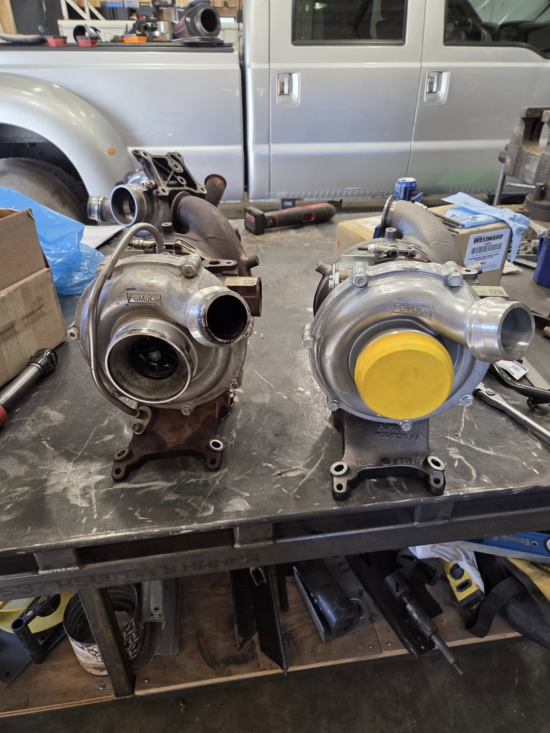 Two turbochargers on a workbench with a vehicle in the background, Cook Automotive.